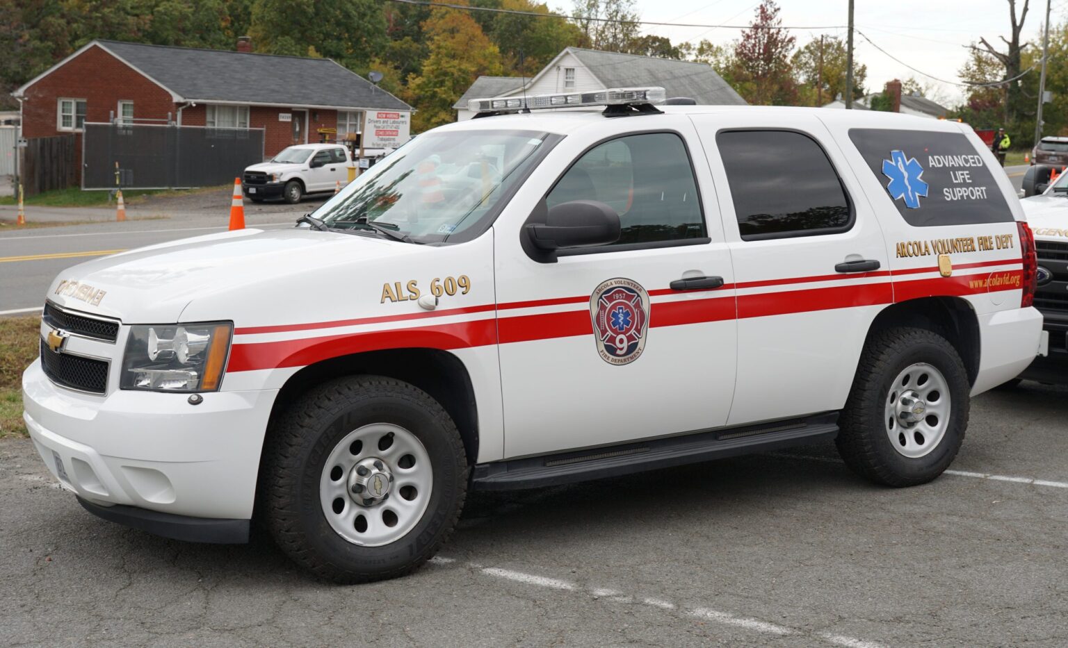 A white SUV marked for advanced life support with red stripes, emergency lights, and the Abilene Volunteer Fire Department logo, parked on a street near buildings and trees.
