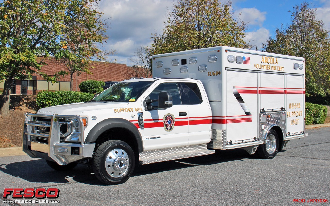 White Angolia Volunteer Fire Dept. support truck with red stripes, parked outdoors near trees and a brick building on a sunny day. The vehicle is clean and prominently displays department markings.