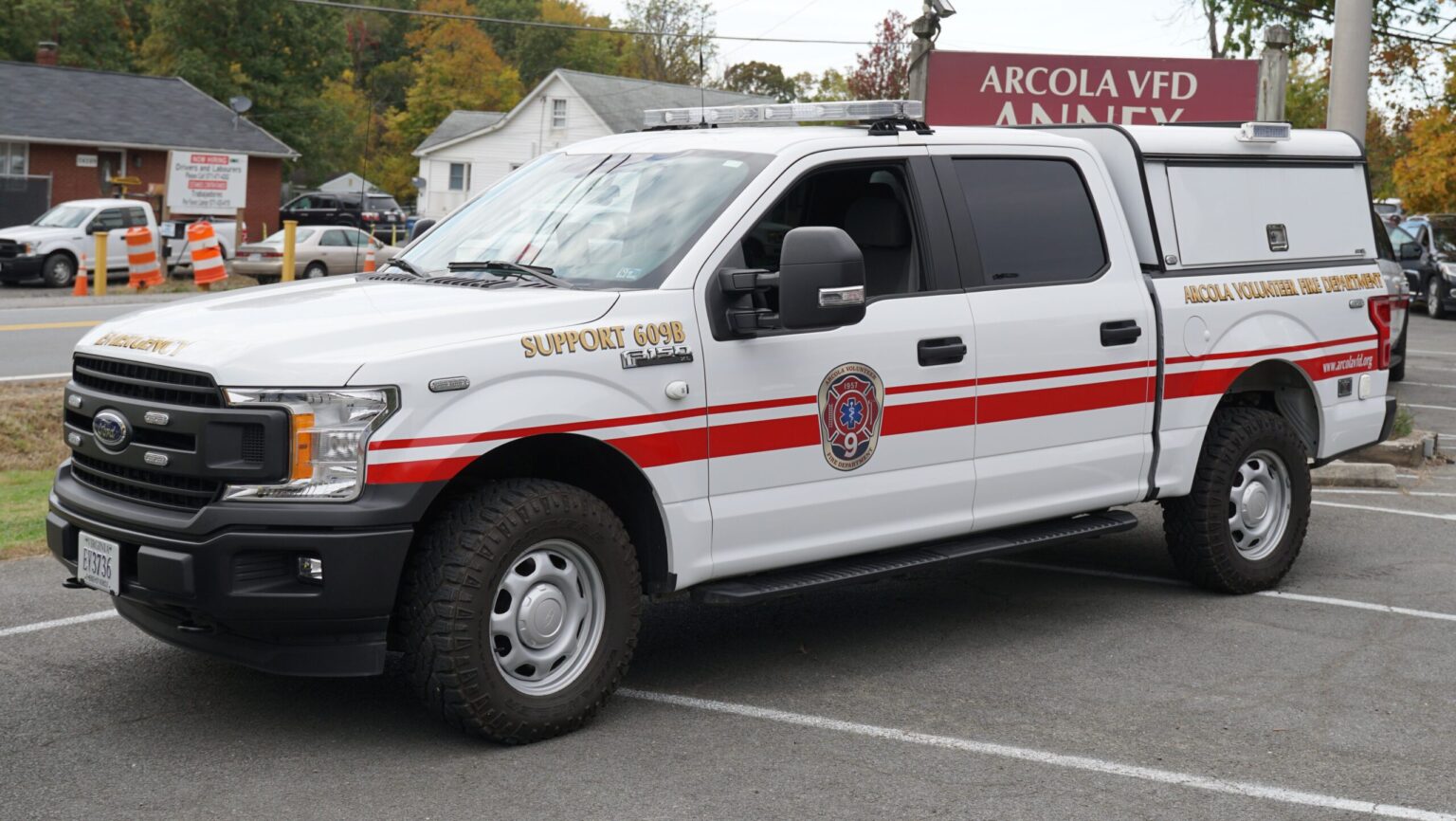 A white pickup truck with red stripes, marked “Arcola Volunteer Fire Department” and “Support 609B,” is parked in front of a building labeled “ARCOLA VFD ANNEX.”.