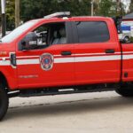 A red Arcola Volunteer Fire Department utility truck with white stripes is parked outside a building. The truck features the department’s logo and “UTILITY 609B” on the side.