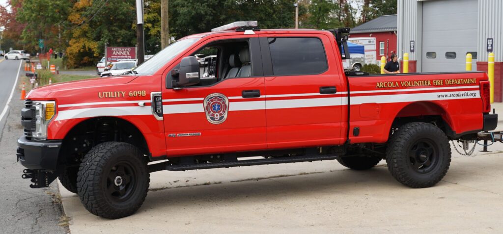 A red Arcola Volunteer Fire Department utility truck is parked outside a building, displaying official markings and fire department insignia.