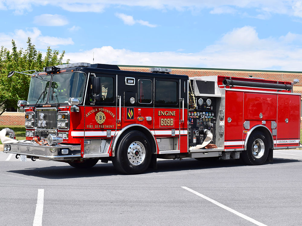 A red and black fire truck with shiny chrome details is parked in a lot on a sunny day. The truck displays “Rescue Volunteer Fire Department” and “Engine 609B” on its side.