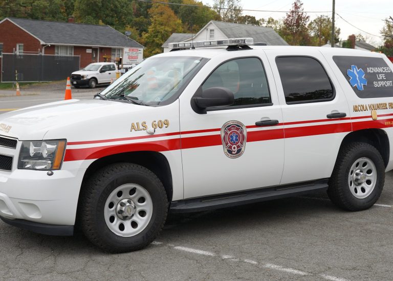 A white SUV marked for advanced life support with red stripes, emergency lights, and the Abilene Volunteer Fire Department logo, parked on a street near buildings and trees.